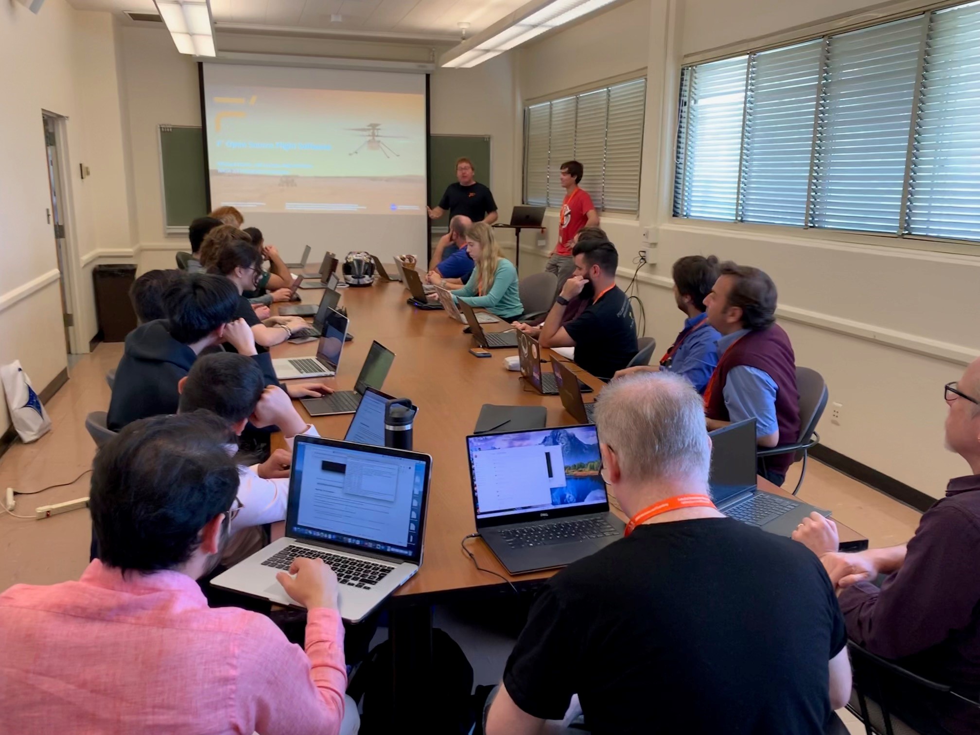 Group of people on their computers in a conference room while a man presents a presentation